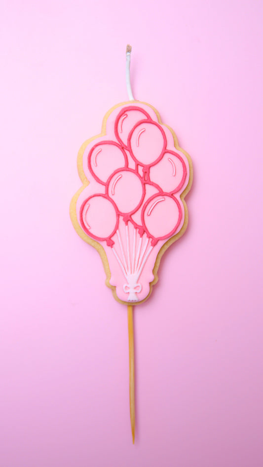 A Cookie Candle of pink ballons on a stick with a pink background