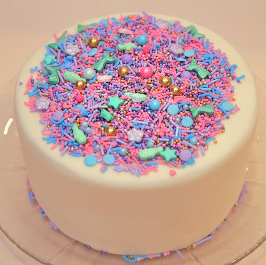White cake with colorful Mermaid sprinkles on a beige background
