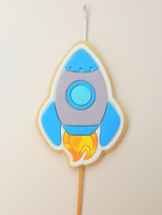 Decorative cookie shaped like a rocket on a stick with blue and gray design.