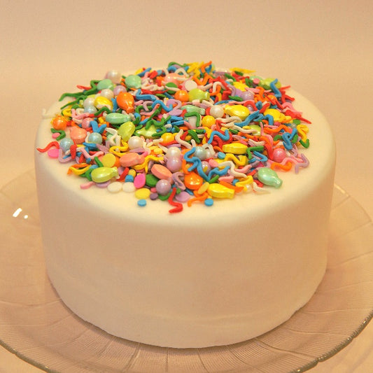 White cake with colorful balloon-shaped sprinkles on a beige background
