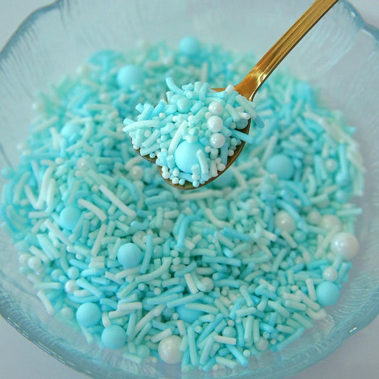 Blue and white sprinkles in a bowl with a gold spoon.