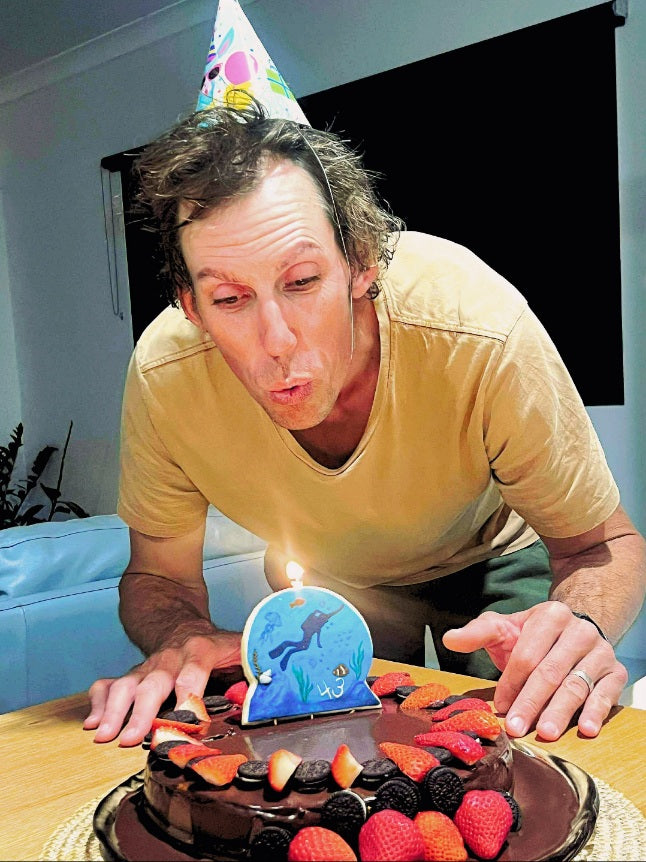 A man wearing a party hat, blowing out the Cookie Candle on his birthday cake. 