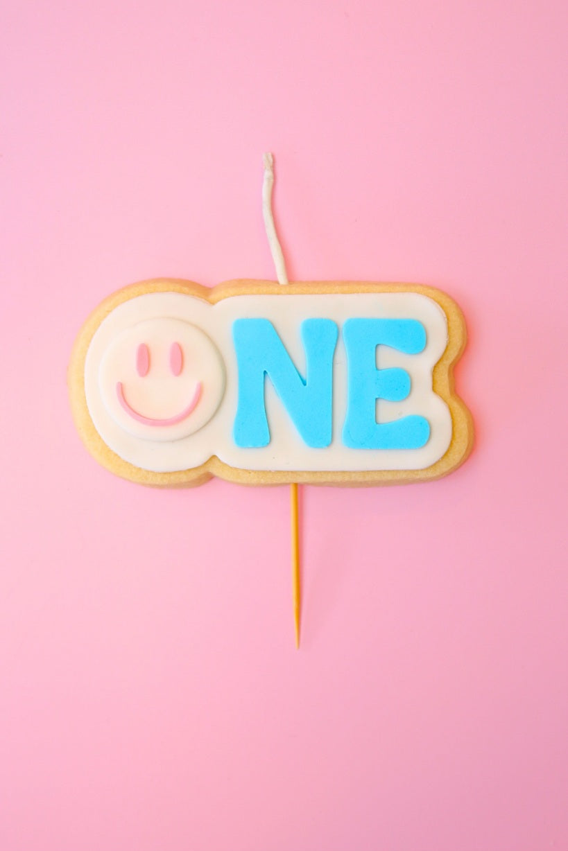 Candle shaped like a smiley face with 'ONE' on a pink background