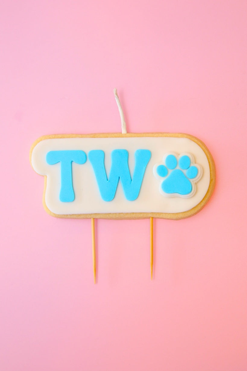 Candle with 'TWO' and paw print on a pink background