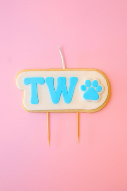 Candle with 'TWO' and paw print on a pink background