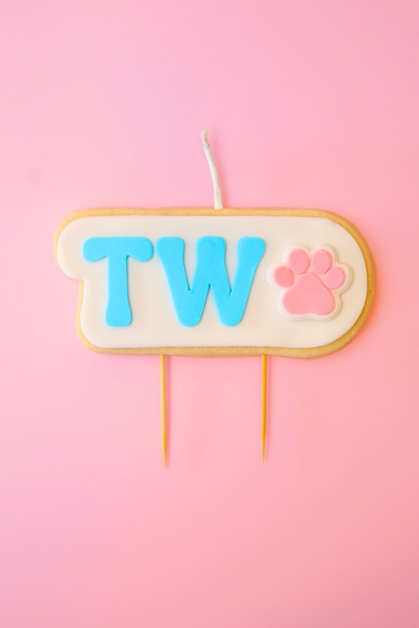 Candle with 'TWO' and a paw print on a pink background
