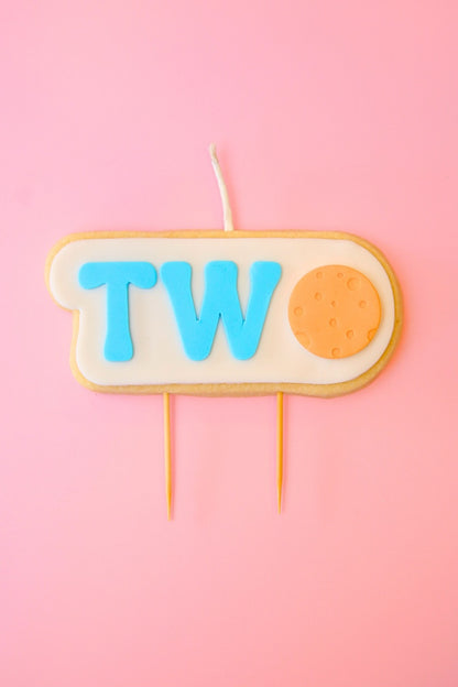 Candle shaped like the number ' TWO ' with blue letters and an orange moon with pink background