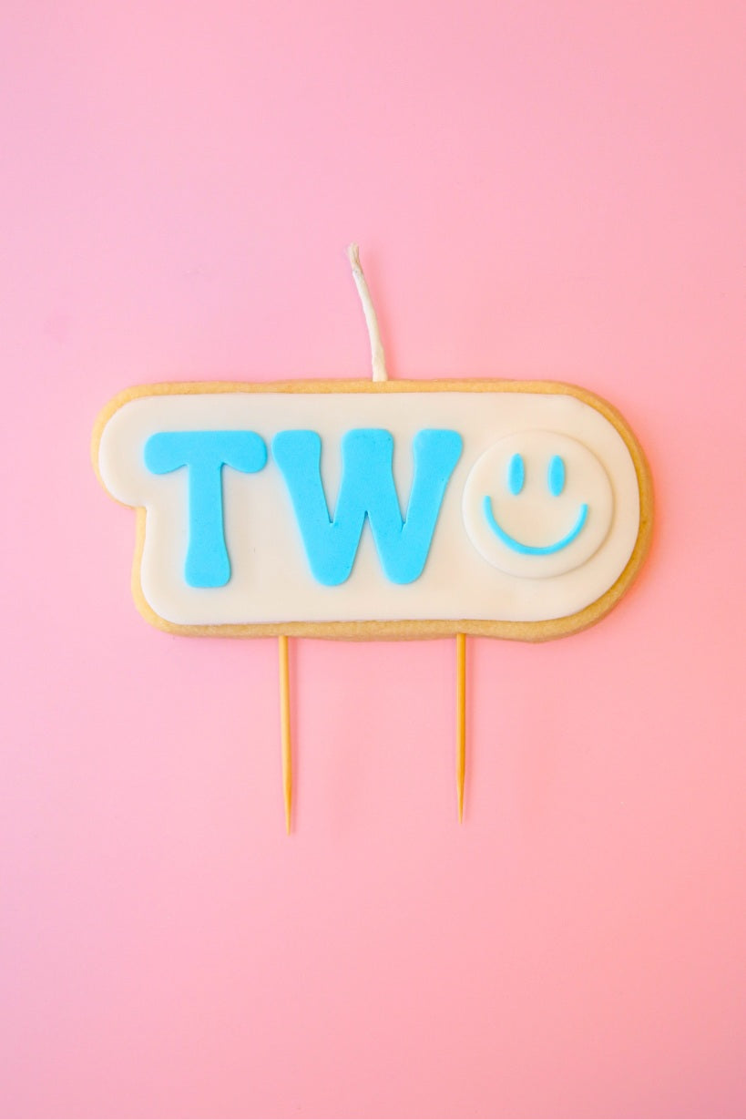 Candle with 'TWO' and smiley face on a pink background