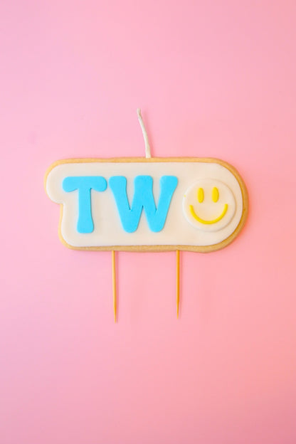 Candle with 'TWO' and a smiley face on a pink background