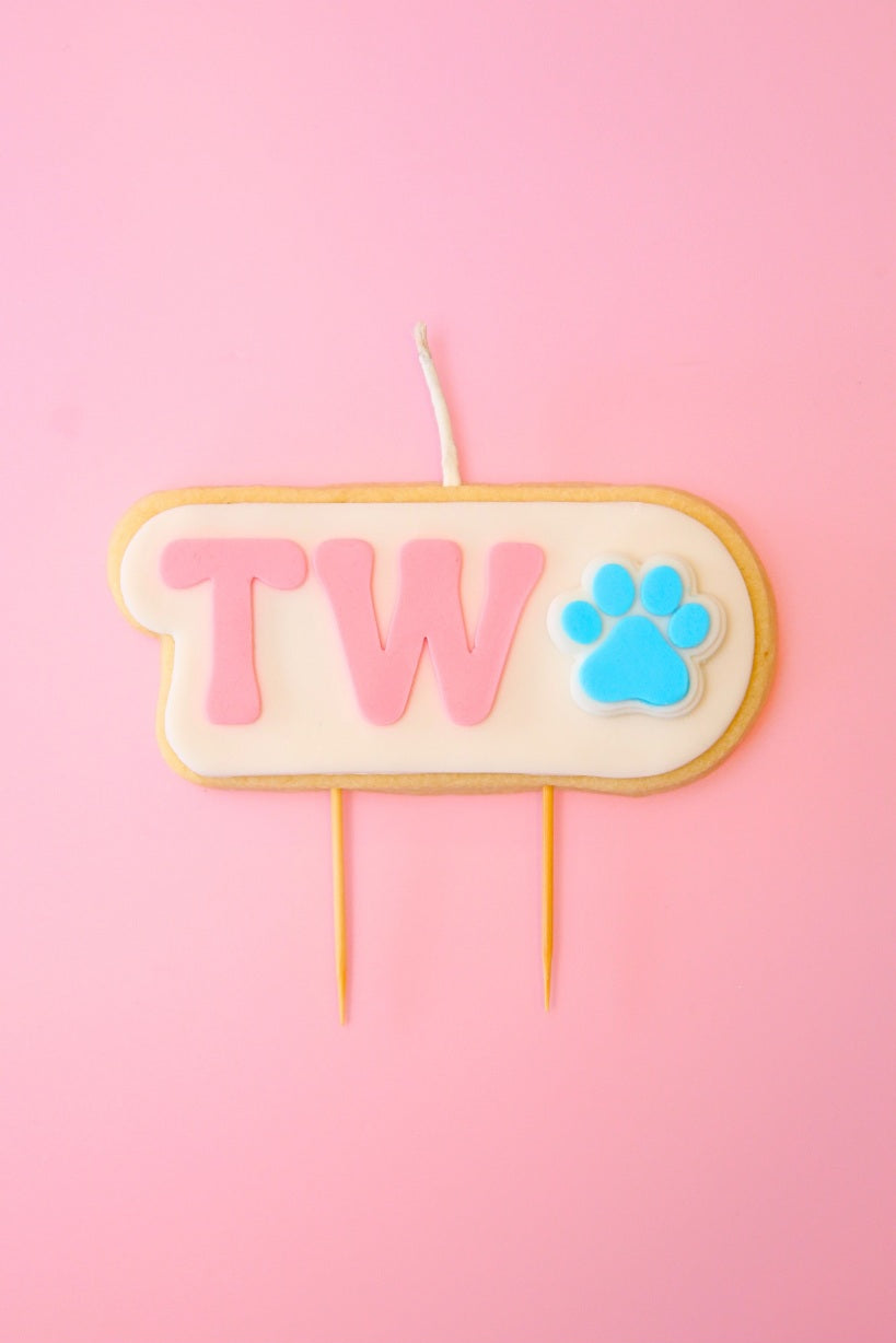 Candle with 'TWO' and a paw print on a pink background