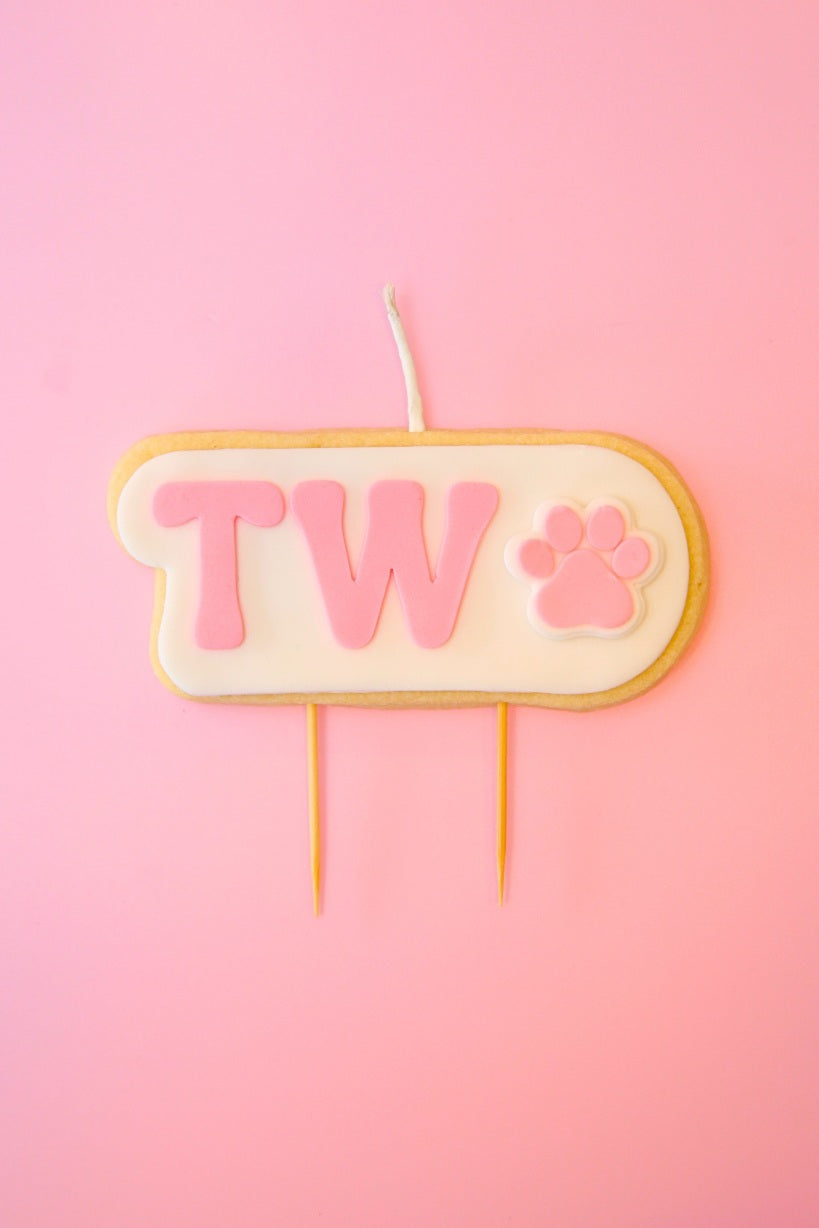 Candle with 'TWO' and paw print on a pink background