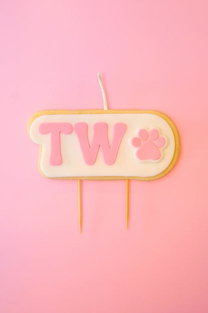 Candle with 'TWO' and paw print on a pink background