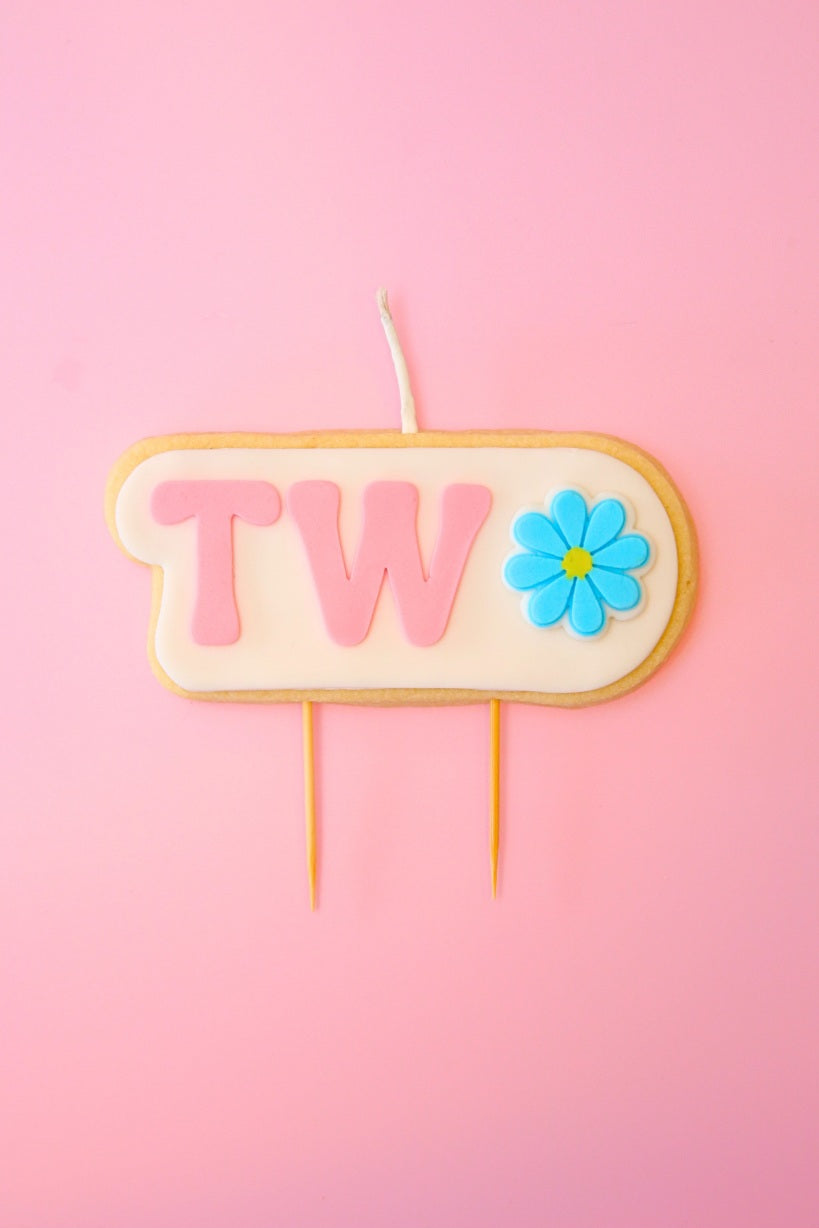 Candle with 'TWO' and a flower on a pink background