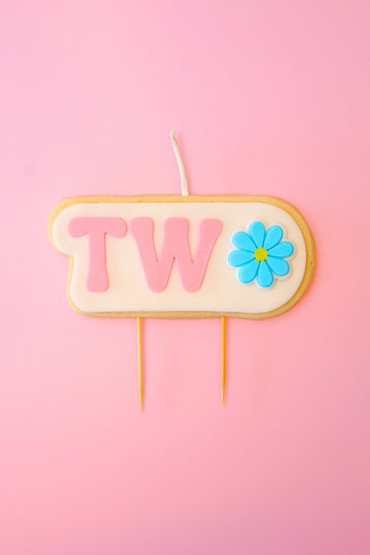 Candle with 'TWO' and a flower on a pink background