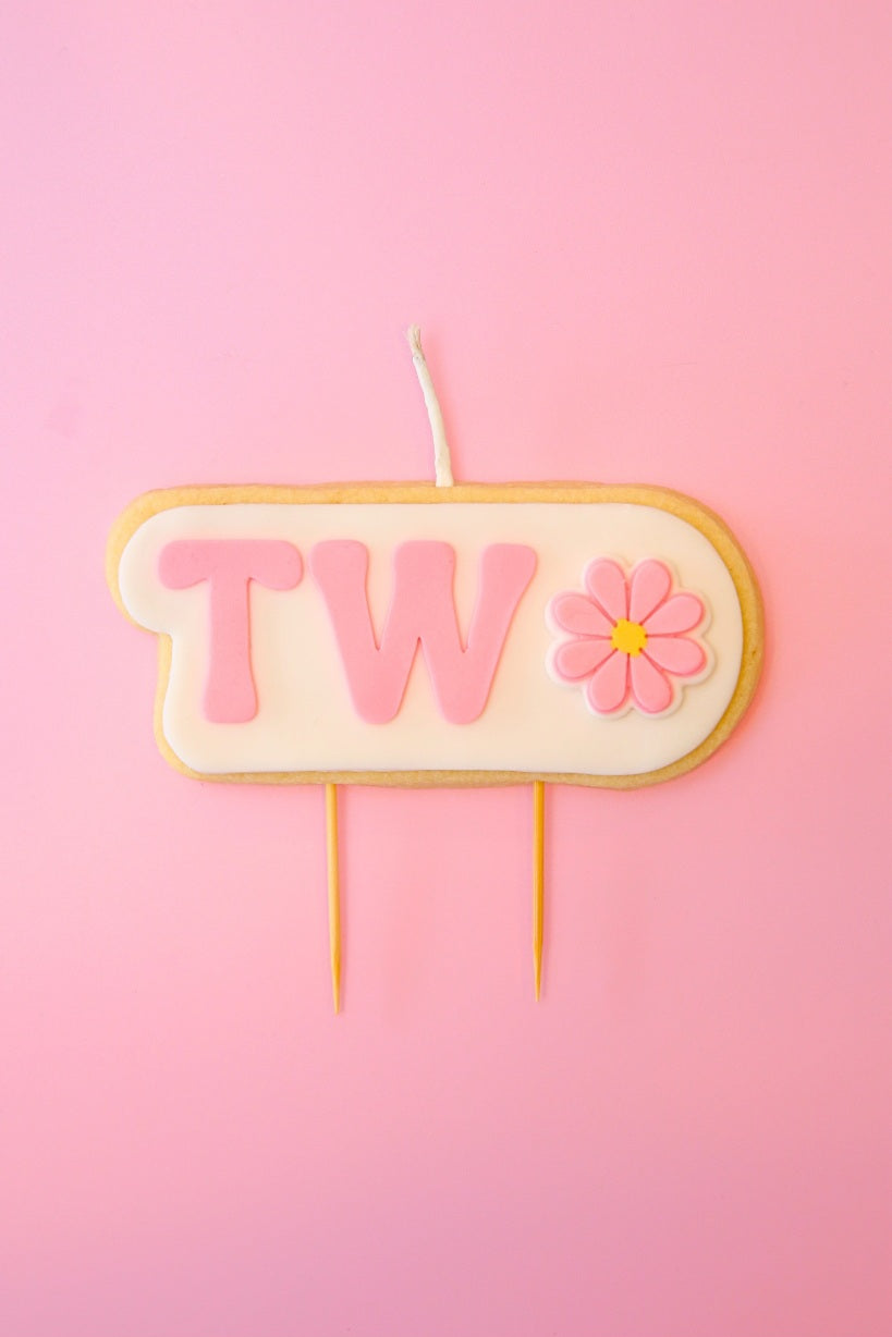 Candle with 'TWO' and a flower on a pink background