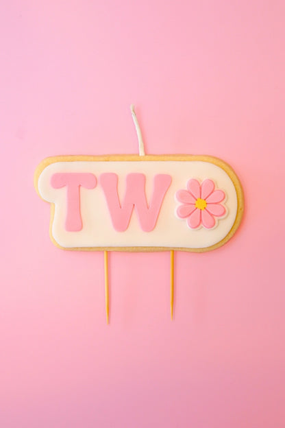 Candle with 'TWO' and a flower on a pink background