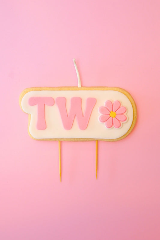 Candle with 'TWO' and a flower on a pink background