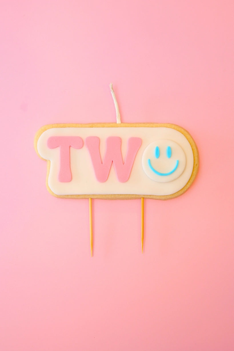 Candle shaped like the number '2' with a smiley face on a pink background