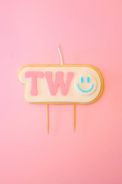 Candle shaped like the number '2' with a smiley face on a pink background