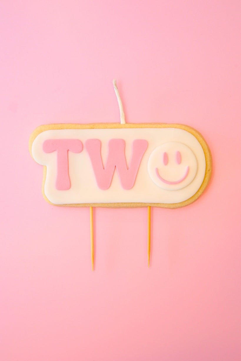 Candle shaped like the number '2' with a smiley face on a pink background