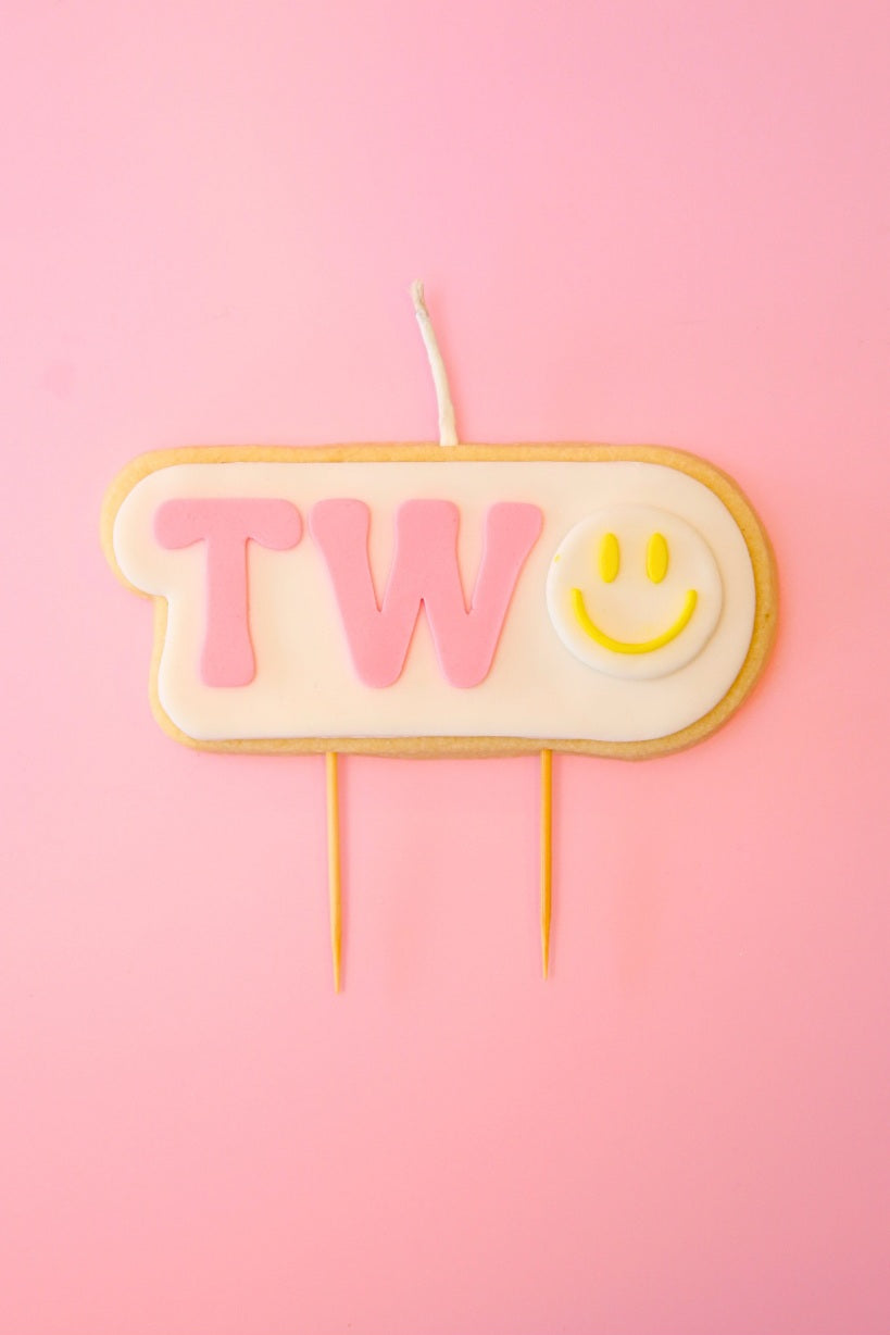 Candle shaped like the number '2' with a smiley face on a pink background