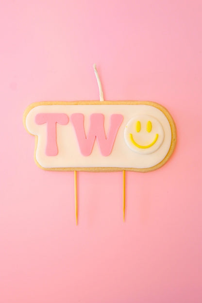 Candle shaped like the number '2' with a smiley face on a pink background