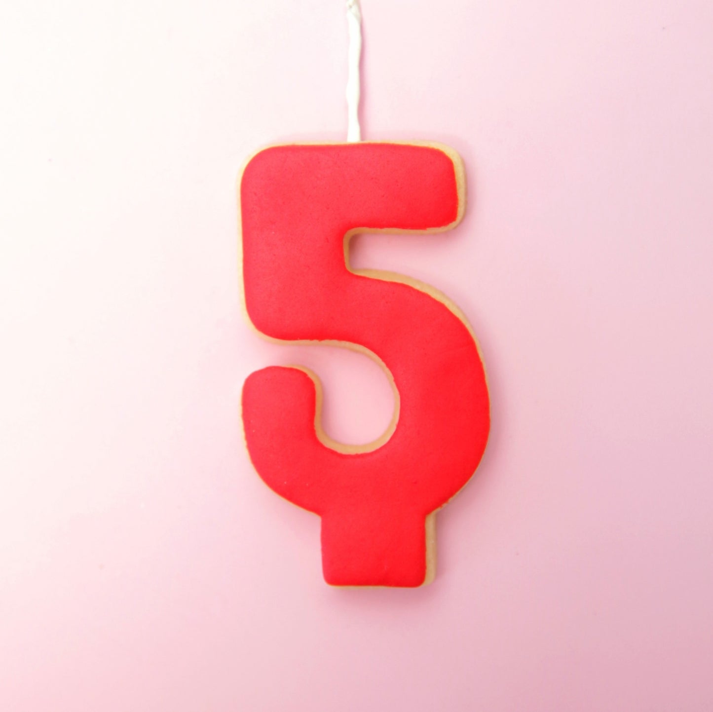 Red number '5' candle cookie on a pink background