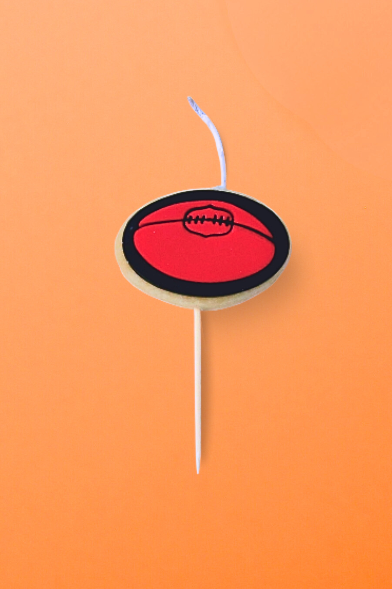 A mini AFL football Cookie Candle on an orange background 