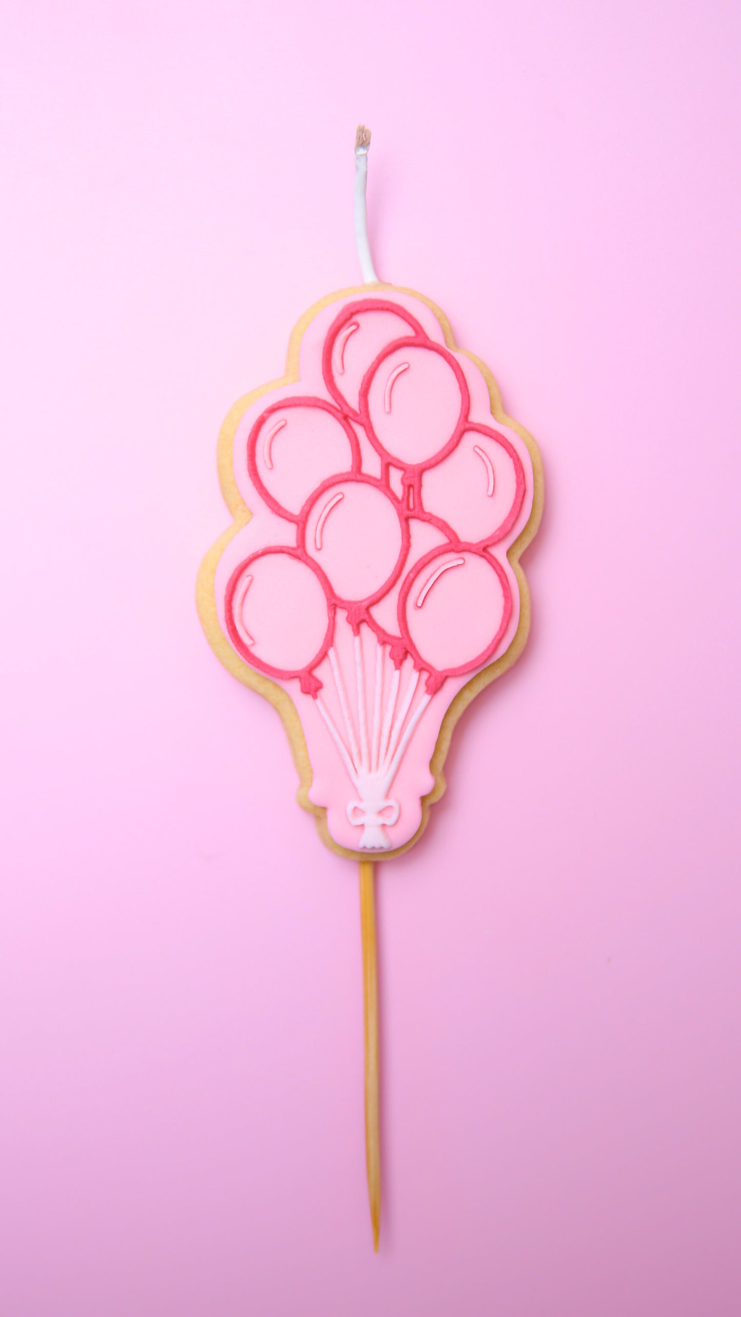 A Cookie Candle of pink ballons on a stick with a pink background