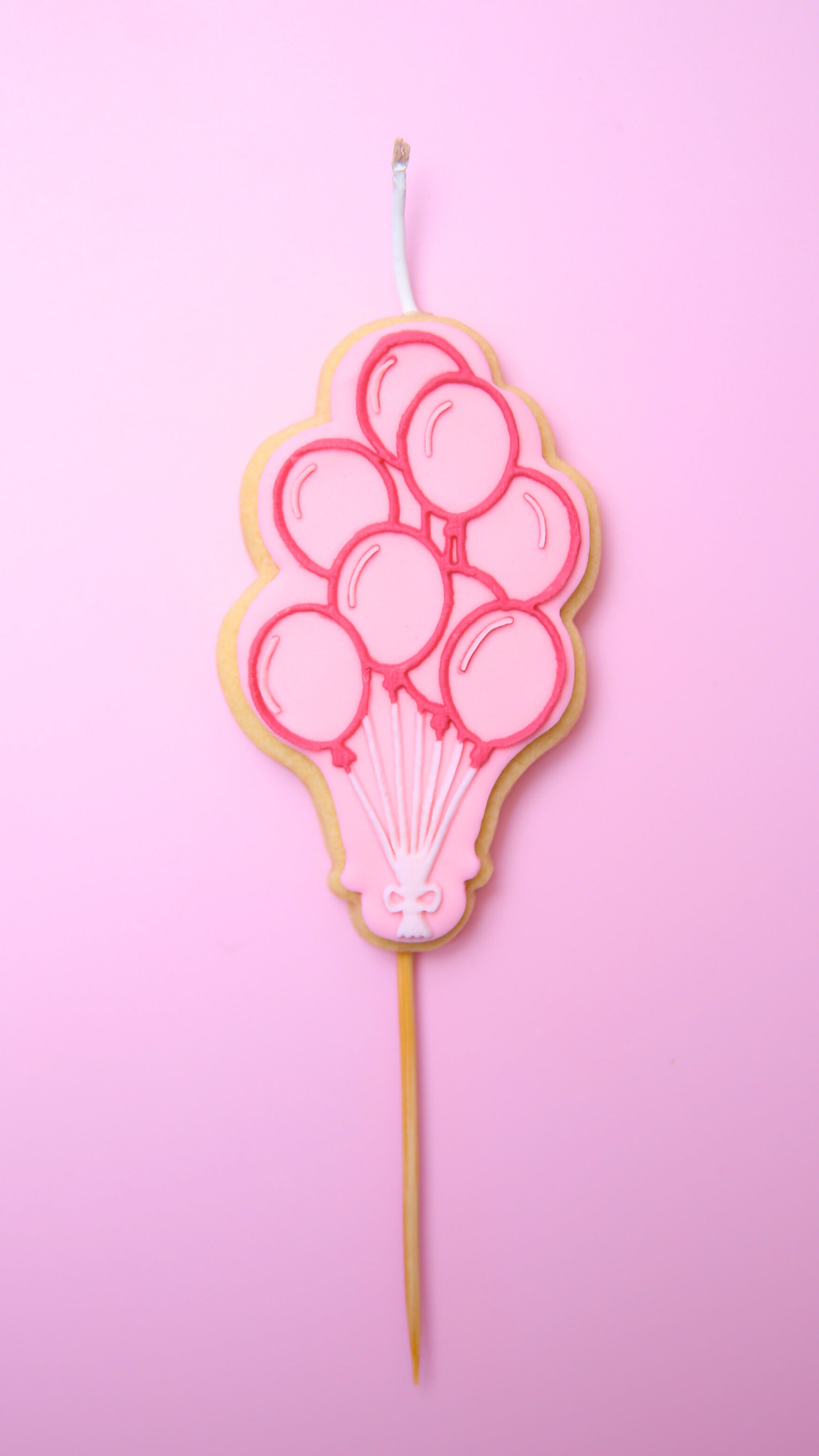 A Cookie Candle of pink ballons on a stick with a pink background