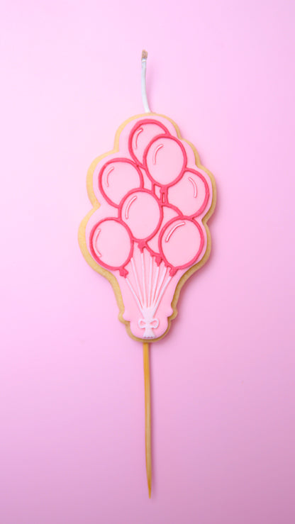 A Cookie Candle of pink ballons on a stick with a pink background