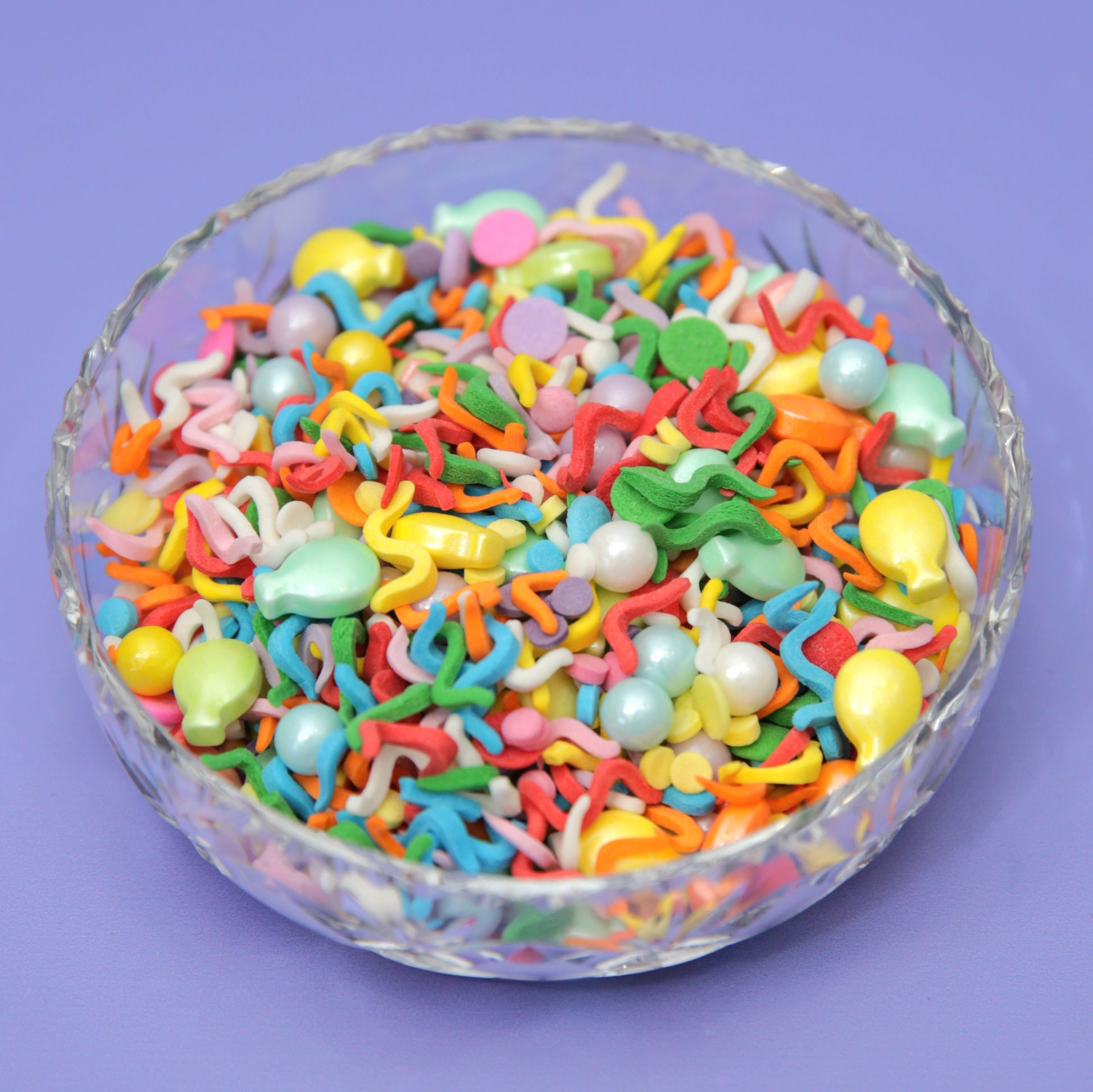 A brightly coloured bowl of wiggly rainbow confetti sprinkles with sugar balloons