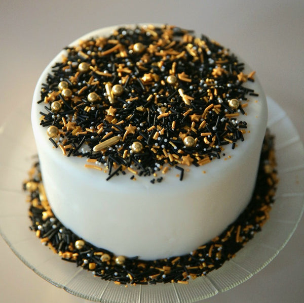 White cake with space themed black and gold sprinkles on a white cake 