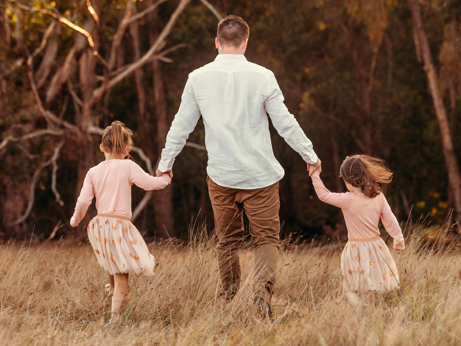 Man and two young girls holding hands in a forest