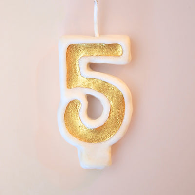Gold number 5 candle on a plain background