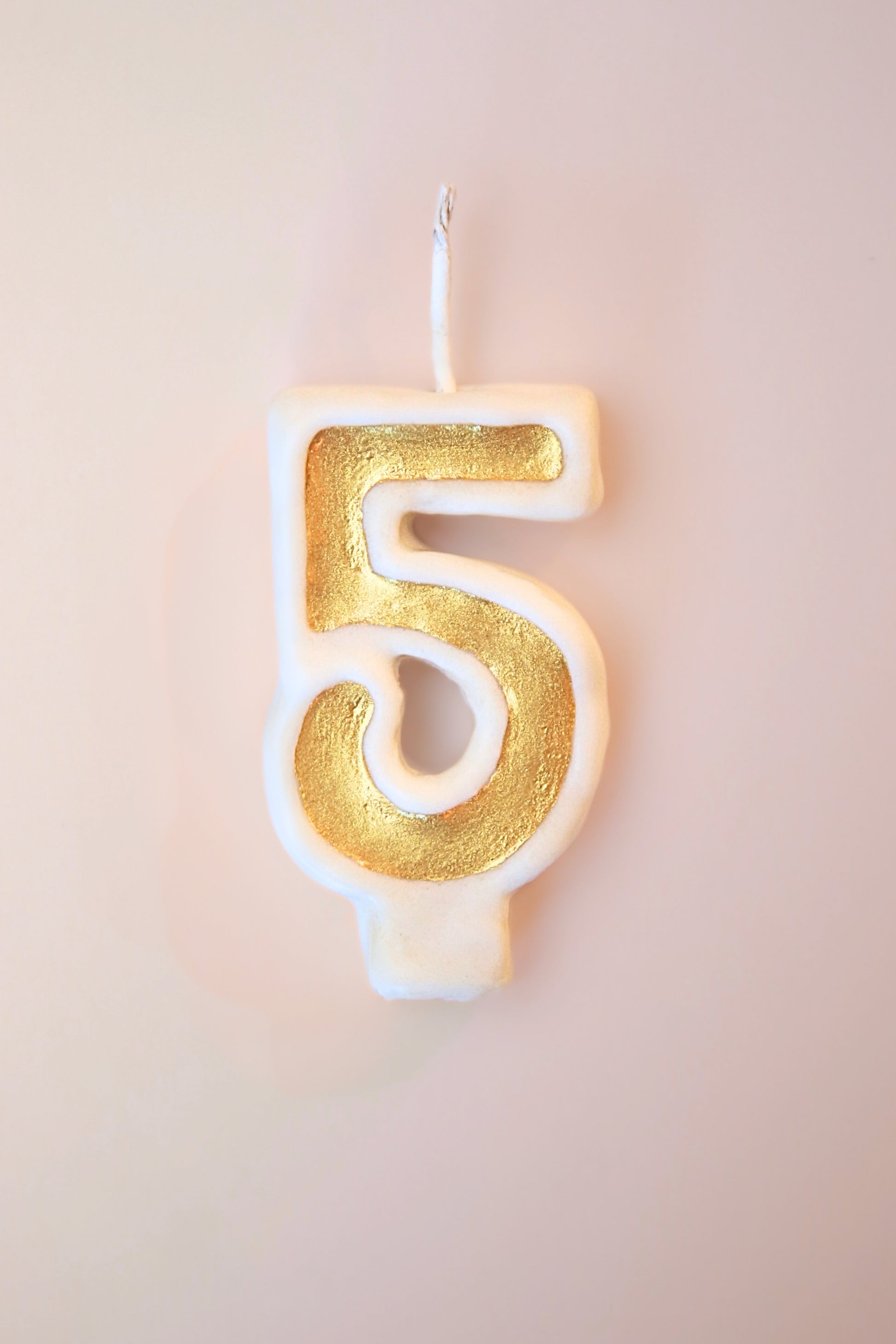 Gold number 5 candle on a plain background