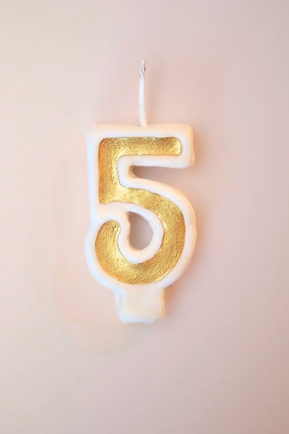 Gold number 5 candle on a plain background