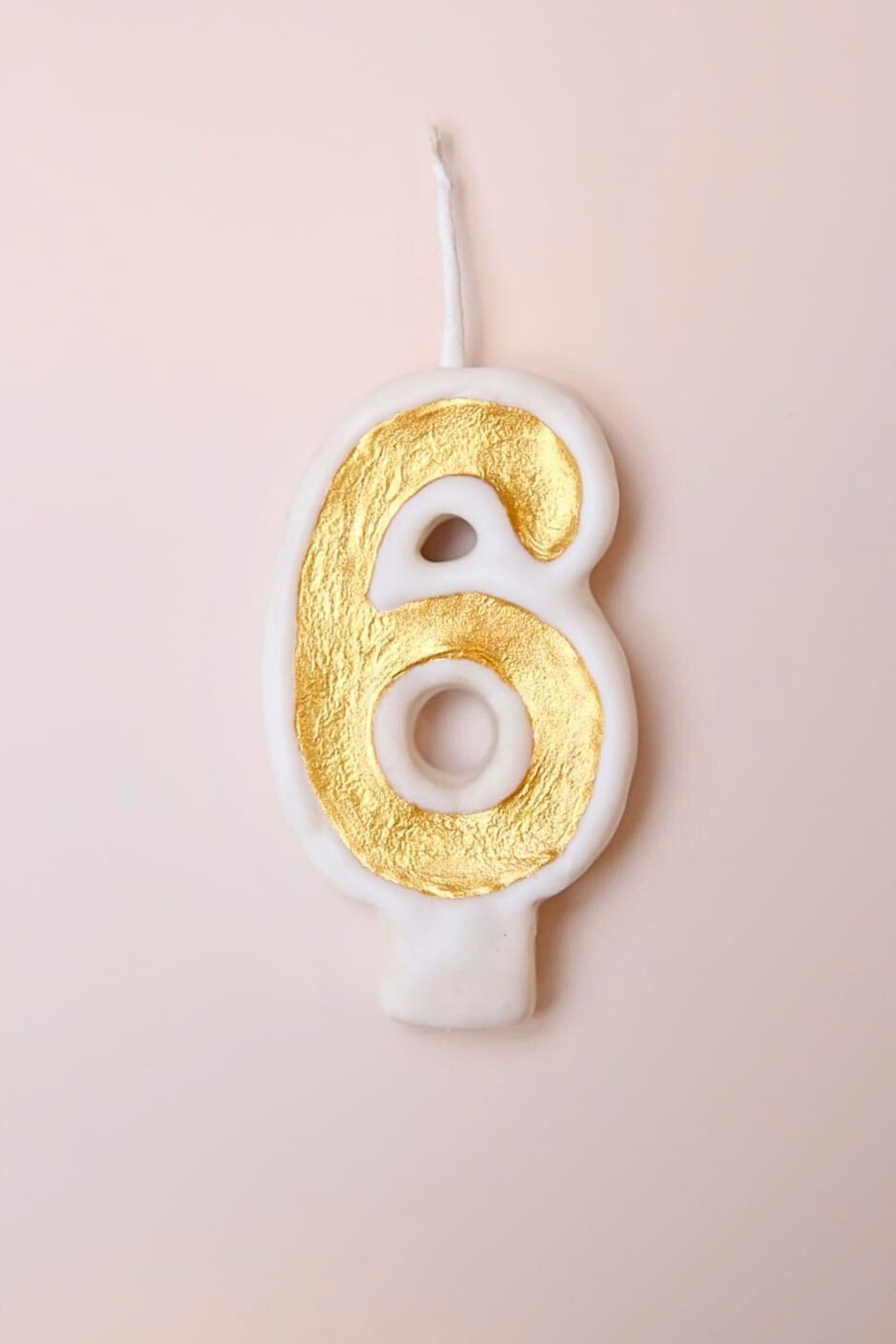 Candle shaped like the number 6 with gold and white design on a light pink background