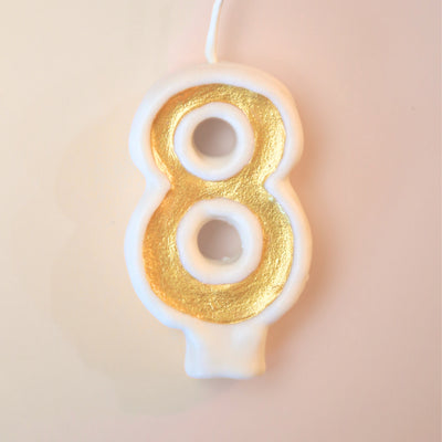Candle shaped like the number 8 with gold and white design on a beige background