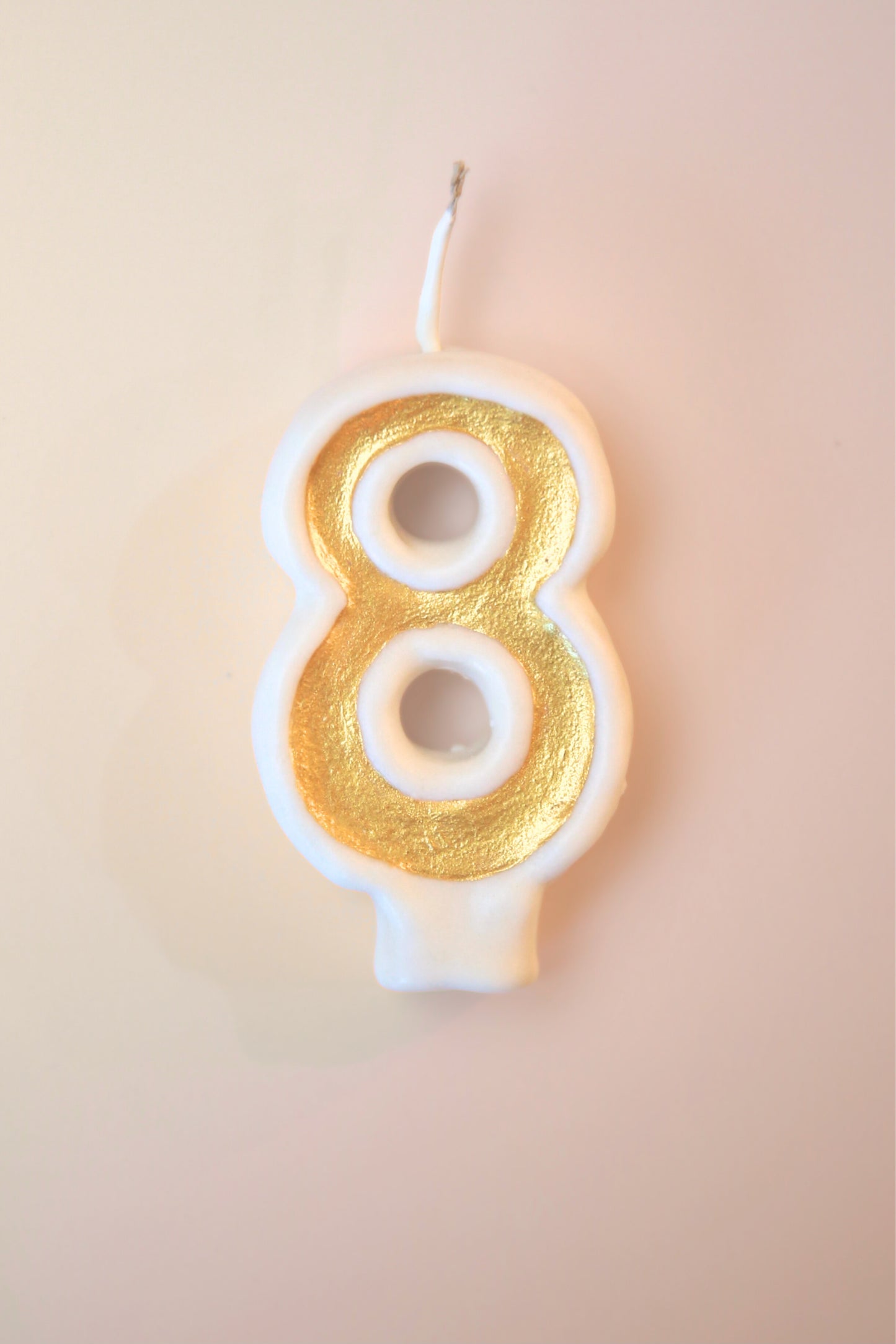 Candle shaped like the number 8 with gold and white design on a beige background