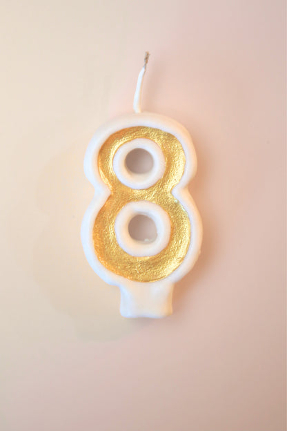 Candle shaped like the number 8 with gold and white design on a beige background
