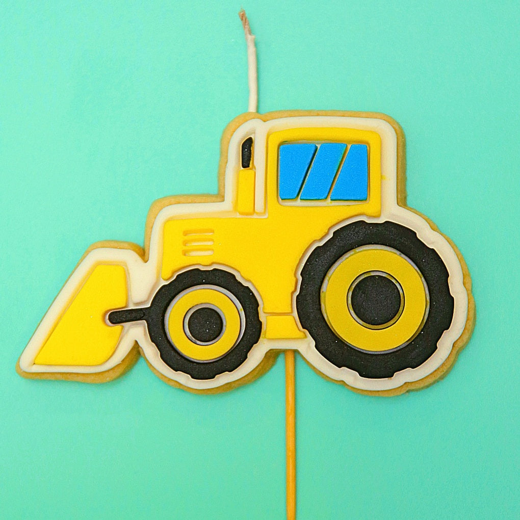 Yellow tractor Cookie Candle on a stick against a teal background