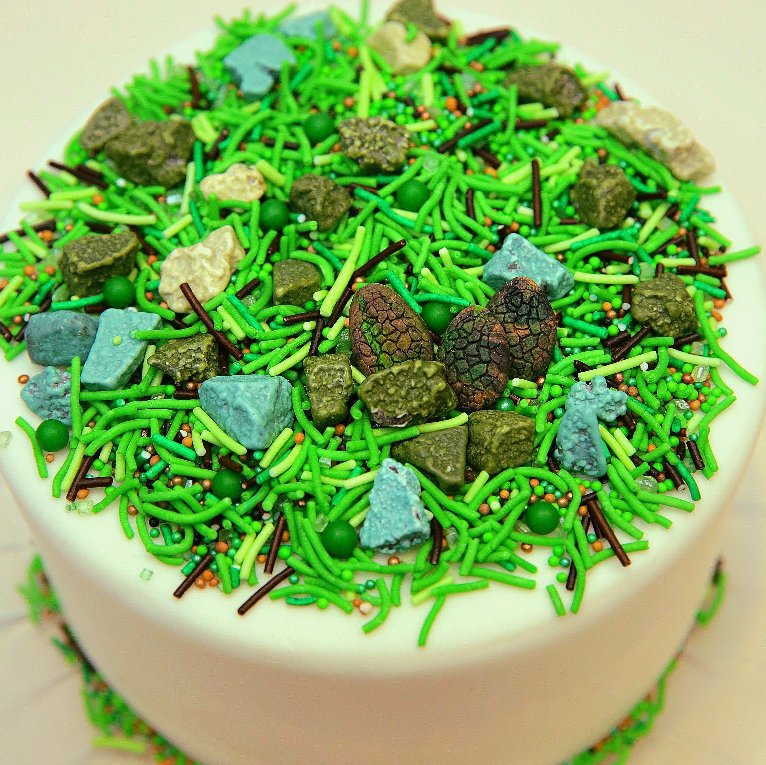 Cake decorated with green and brown sprinkles resembling grass and rocks on a white cake 
