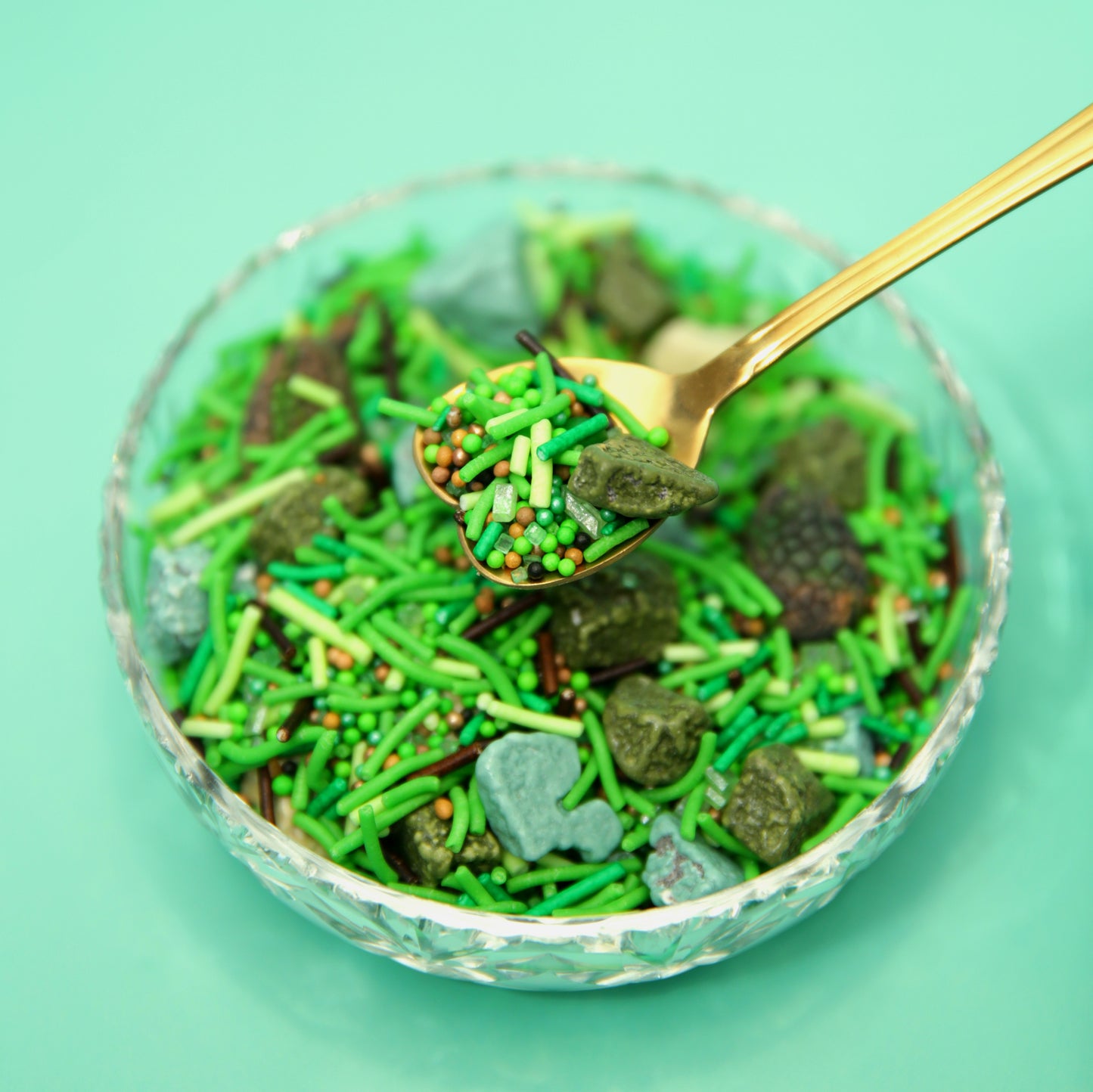 Glass bowl filled with green and brown sprinkles with chocolate rocks on a light green background