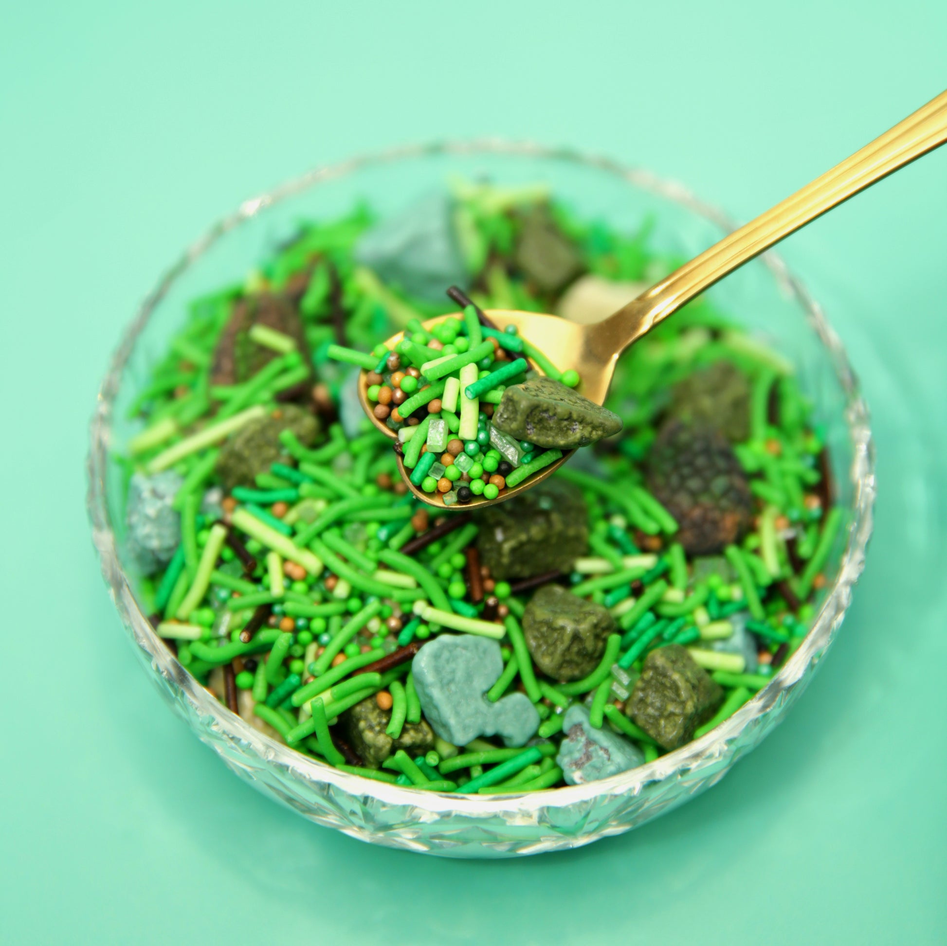 Glass bowl filled with green and brown sprinkles with chocolate rocks on a light green background
