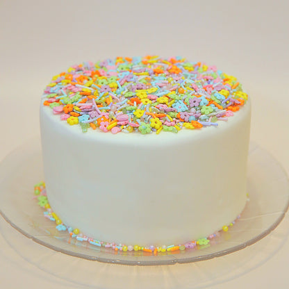 White cake with colourful sprinkles on a clear plate against a white background