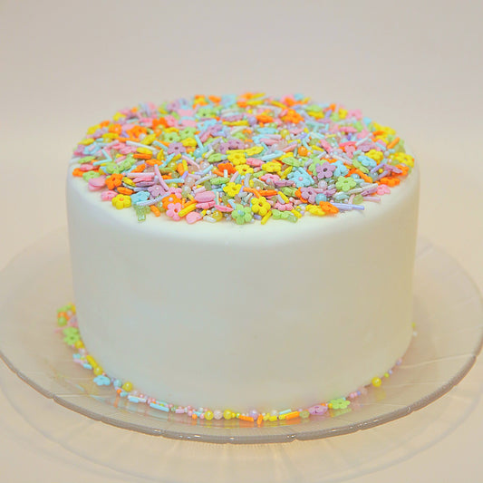 White cake with colourful sprinkles on a clear plate against a white background