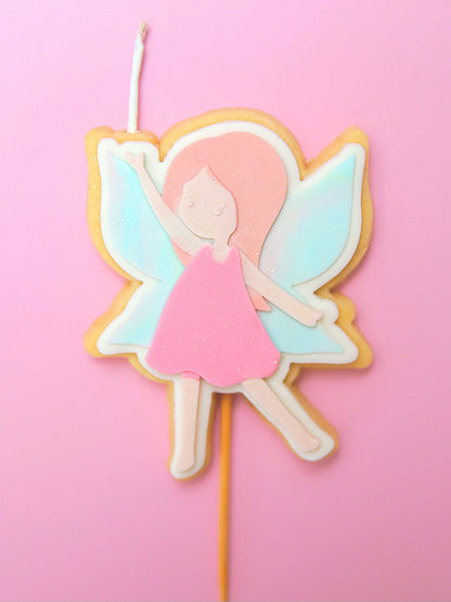 Fairy-themed cookie on a stick and wick with pastel colours and glitter against a pink background