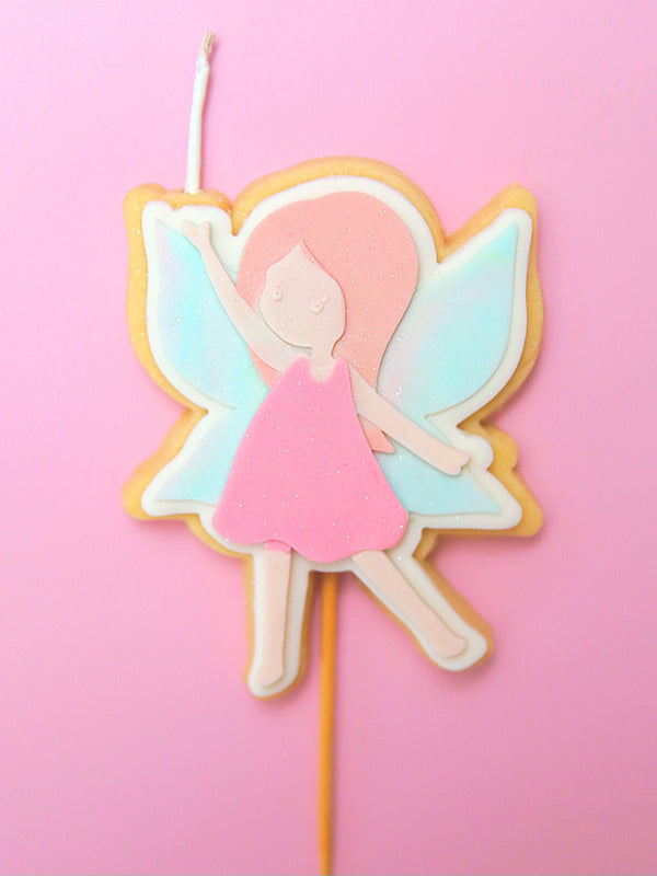 Fairy-themed cookie on a stick and wick with pastel colours and glitter against a pink background