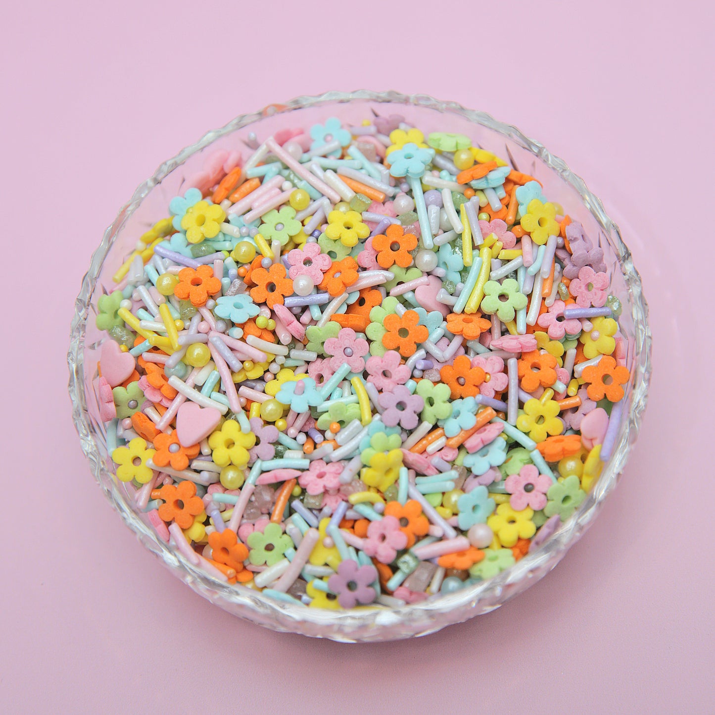 Pastel-colored flower-shaped sprinkles in a glass bowl on a pink background